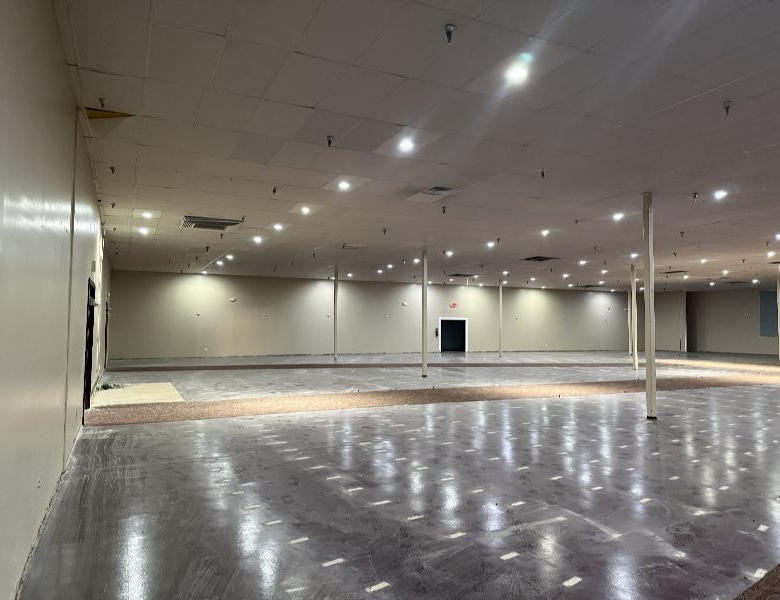 Empty indoor retail or showroom space with a polished concrete floor, beige walls, and evenly spaced ceiling lights.