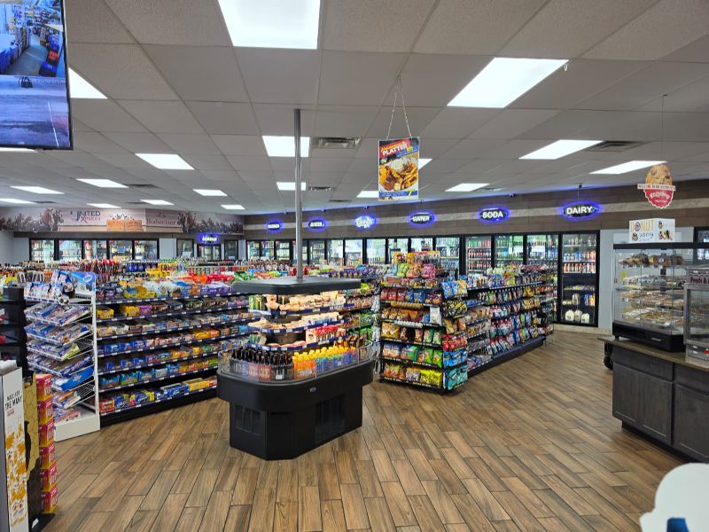 Bright supermarket interior with central checkout island and long aisles of snacks and beverages.