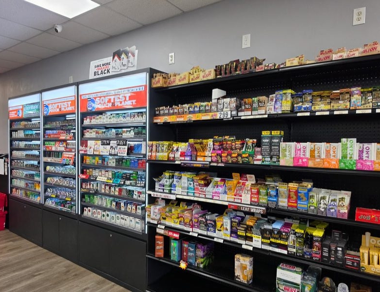Grocery store aisle with three tall refrigerated display cases on the left and shelves of assorted packaged goods on the right.