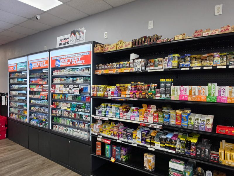 Grocery store aisle with three tall refrigerated display cases on the left and shelves of assorted packaged goods on the right.