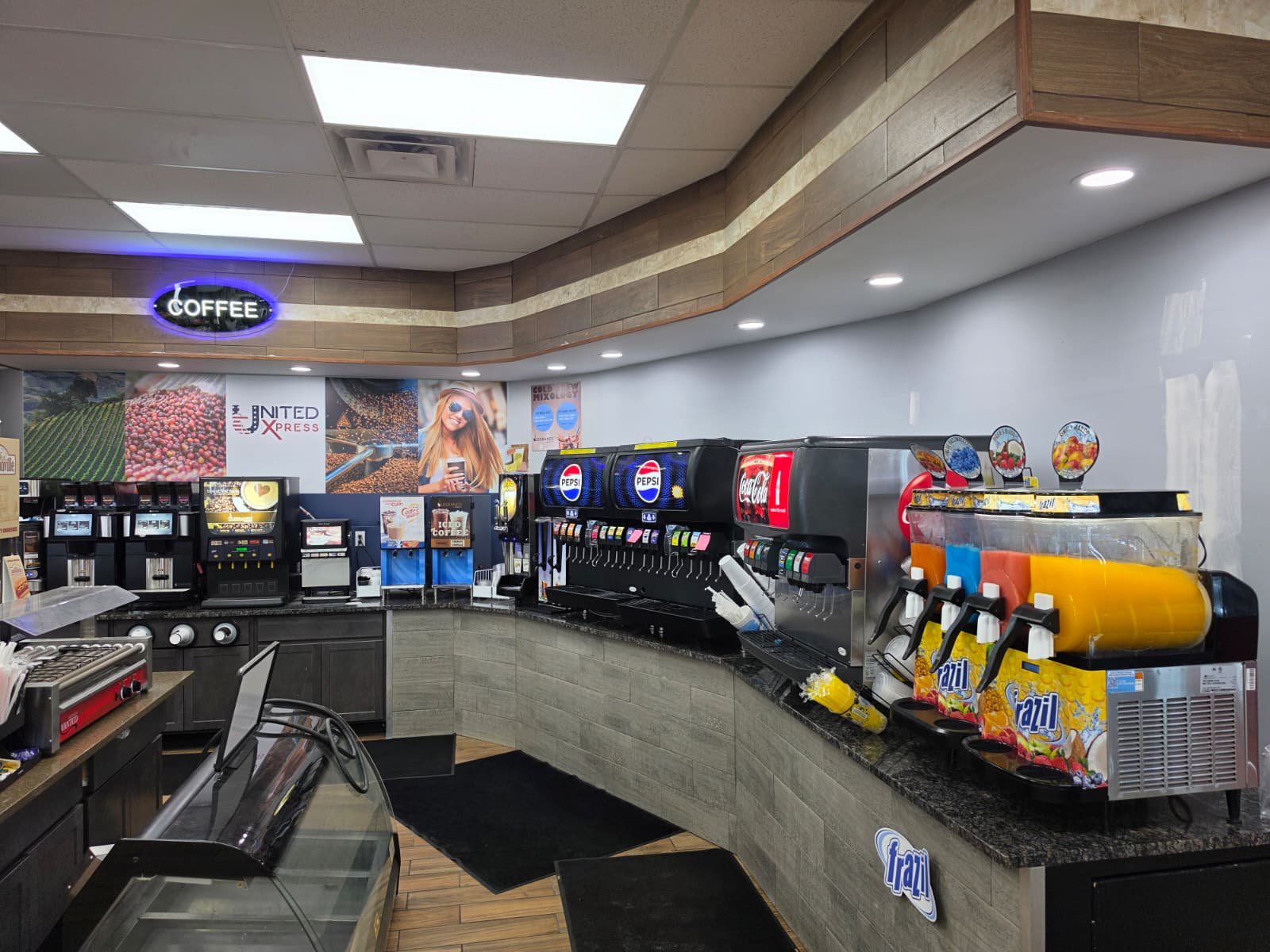Cafe counter with self-serve beverage machines, including Pepsi and Coca-Cola taps, and juice dispensers under a neon COFFEE sign.