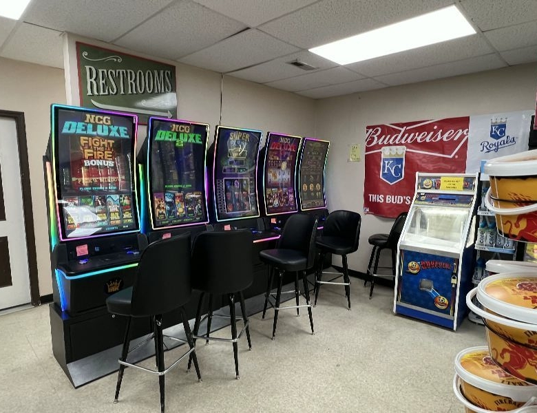 Row of colorful arcade game machines with black stools along a beige wall.