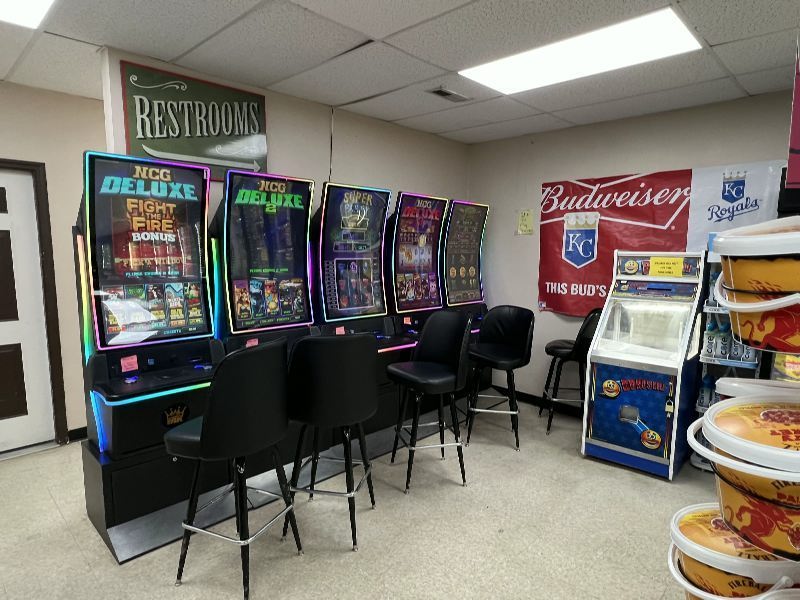 Row of colorful arcade game machines with black stools along a beige wall.