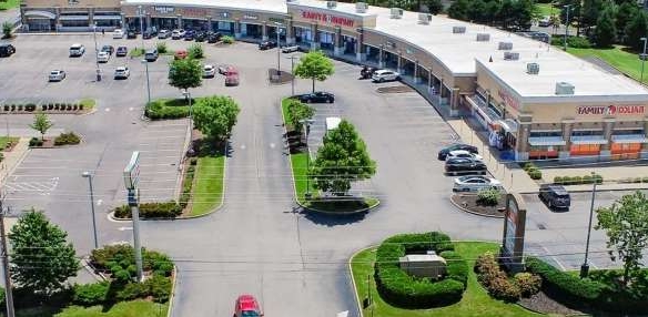Aerial view of a curved-shopping-plaza with storefronts, parking lots, and green landscaping.