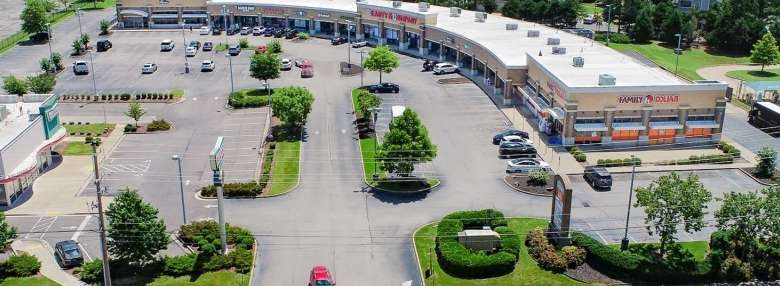 Aerial view of a curved-shopping-plaza with storefronts, parking lots, and green landscaping.