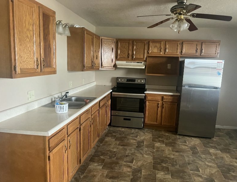 L-shaped kitchen with wooden cabinets, white countertops, and stainless steel fridge and range.