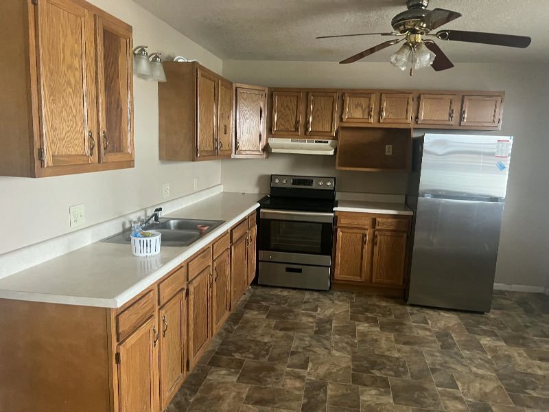 L-shaped kitchen with wooden cabinets, white countertops, and stainless steel fridge and range.