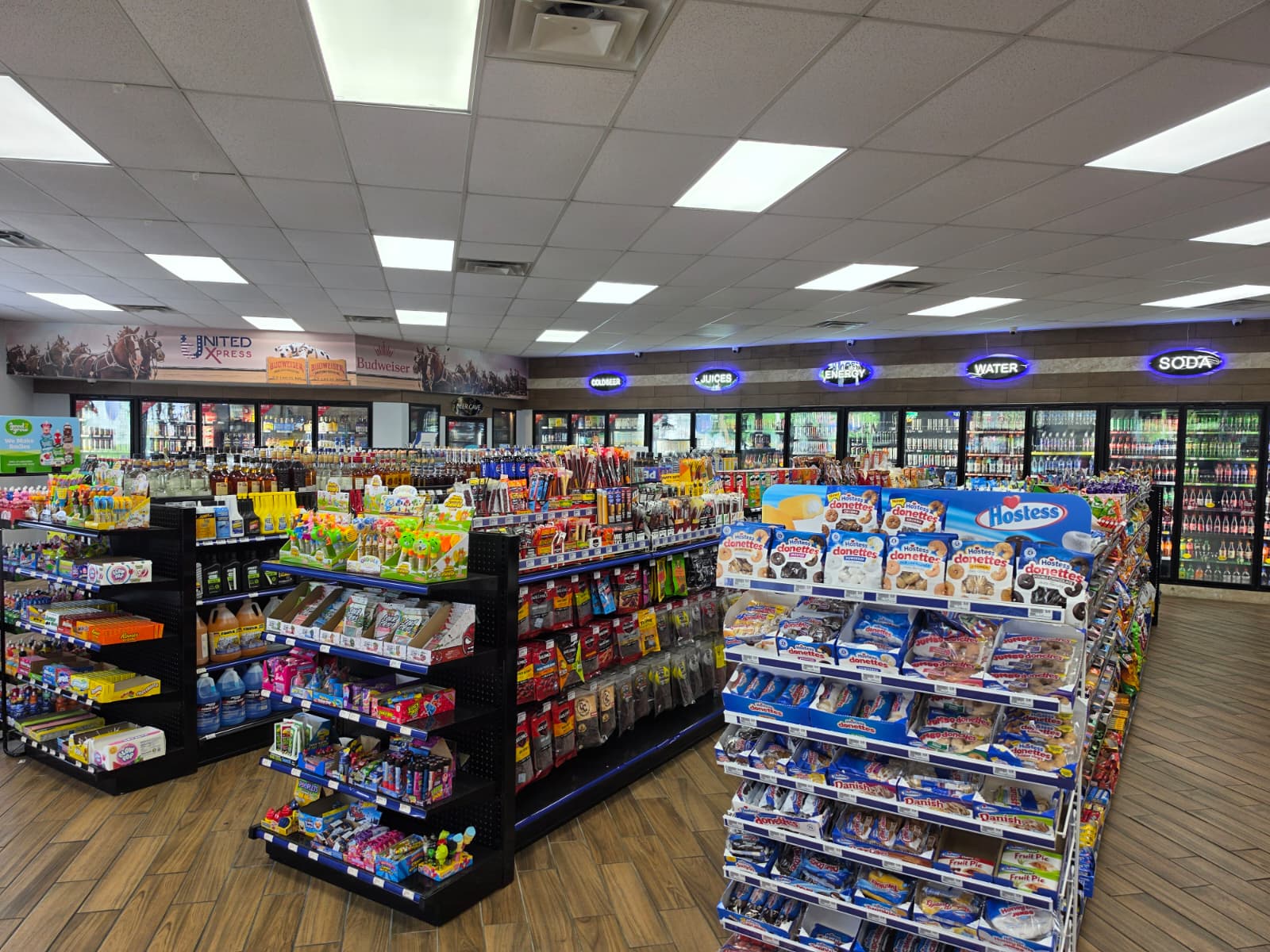Bright store interior with multiple shelves of snacks in the foreground and refrigerated drinks along the back wall.