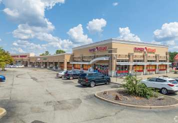 Strip mall with multiple storefronts and cars parked in the lot on a sunny day.