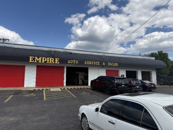 Auto service shop storefront with black awning reading 'Empire Auto Service & Sales' and red garage doors; cars parked in front on a sunny day.