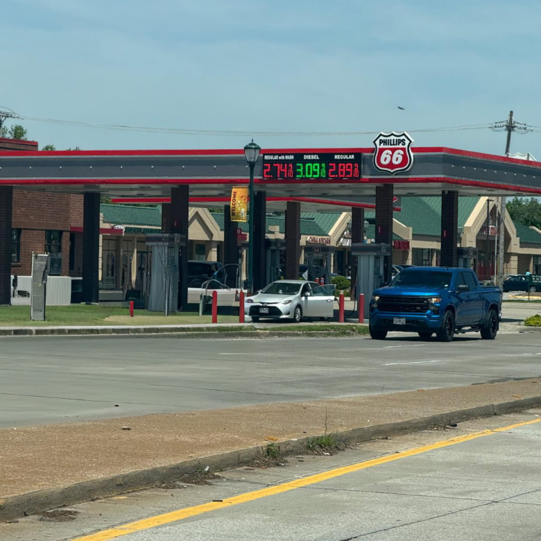 Gas station with Phillips 66 sign and a digital fuel-price board; vehicles at the pumps under a red-and-gray canopy.