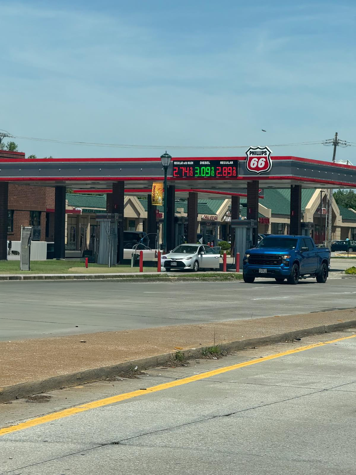 Gas station with Phillips 66 sign and a digital fuel-price board; vehicles at the pumps under a red-and-gray canopy.