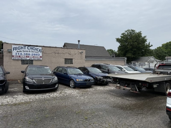 Used car lot with multiple sedans parked in front of a small dealership building and a flatbed trailer on the right side.