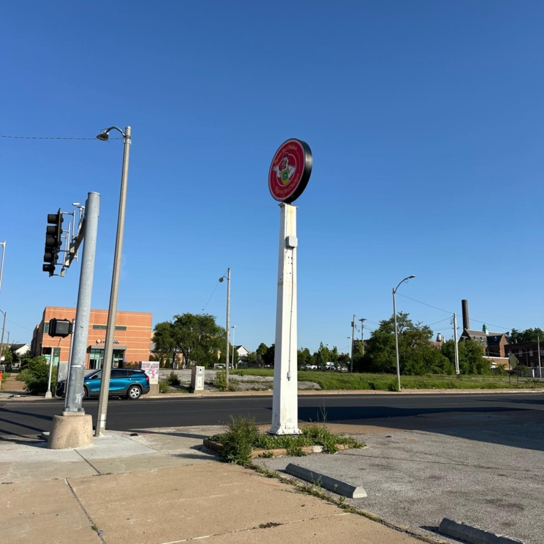 Circular red restaurant sign mounted on a tall white pole in a parking lot, with a clear blue sky and street behind it