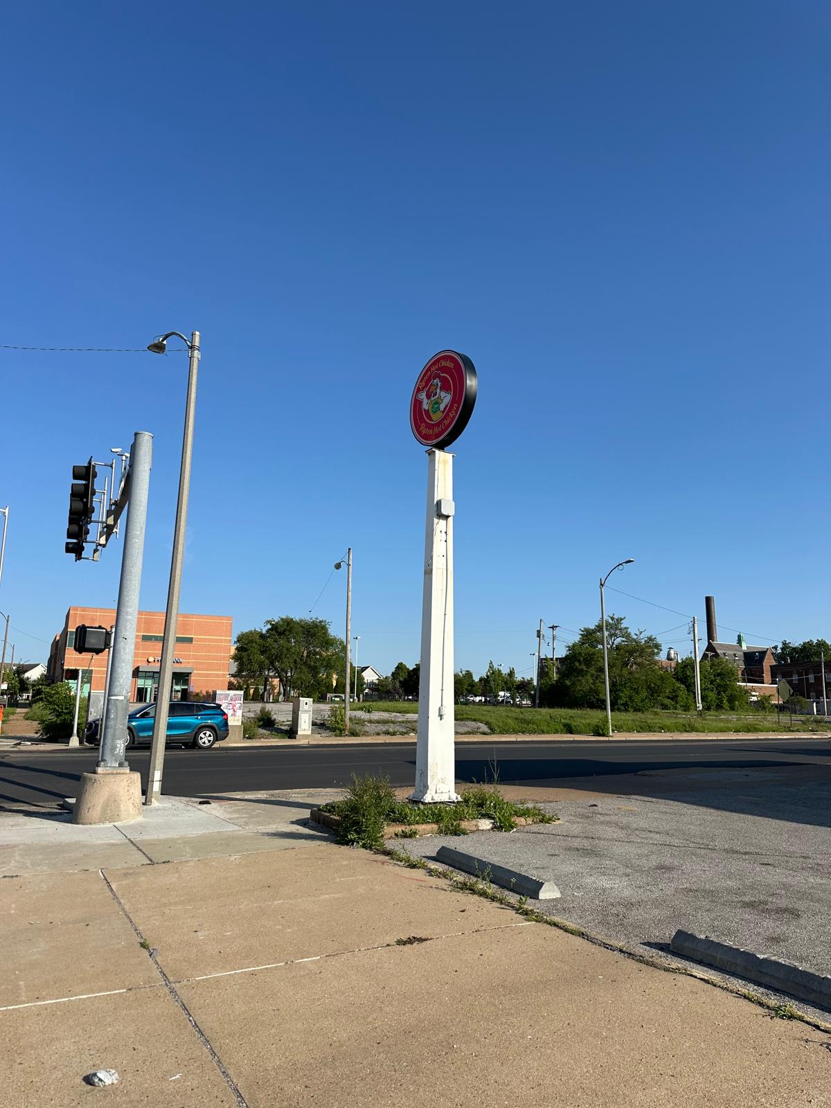 RLXH2727 Circular red restaurant sign mounted on a tall white pole in a parking lot, with a clear blue sky and street behind it