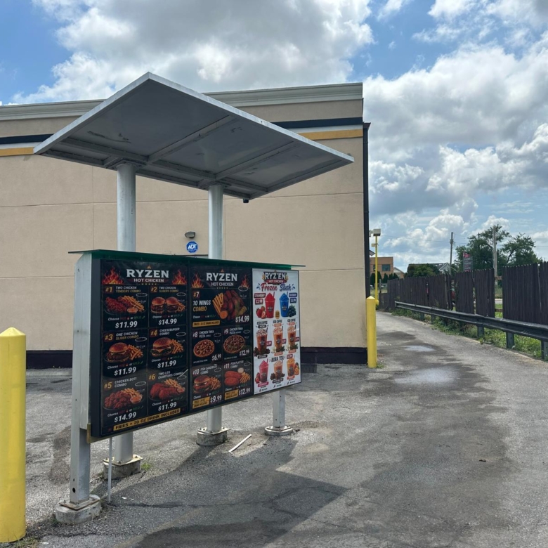 Exterior fast-food menu board labeled 'RYZEN' under a metal canopy in a parking lot.