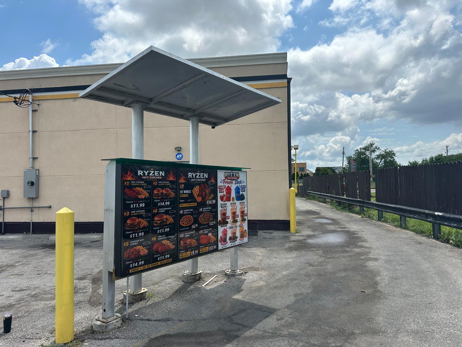 SISL2283 Exterior fast-food menu board labeled 'RYZEN' under a metal canopy in a parking lot.