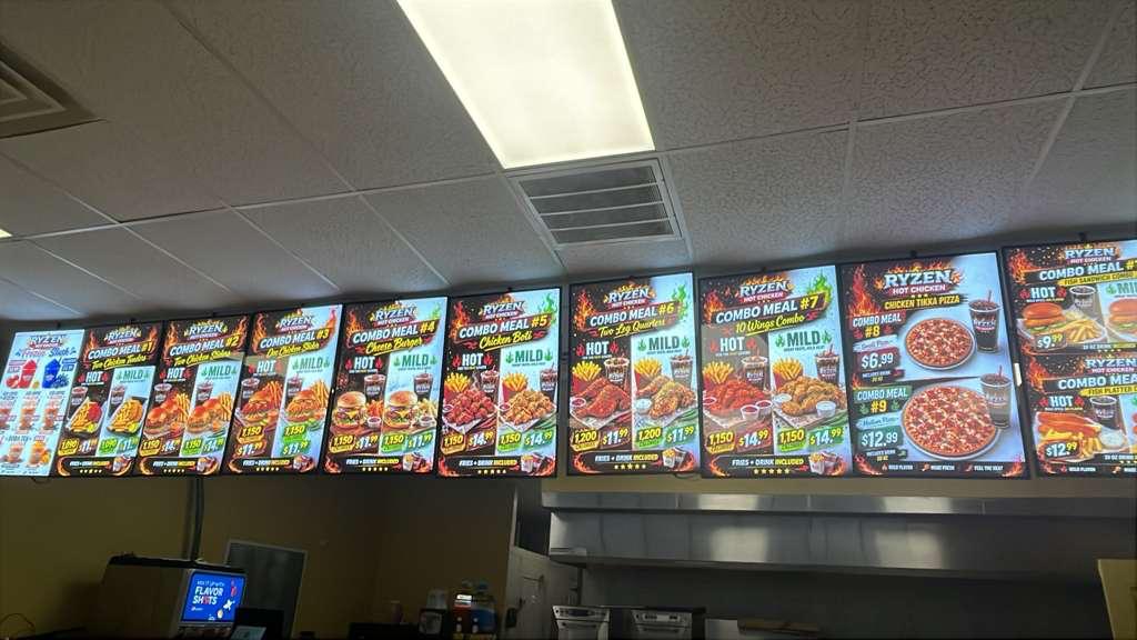 TBNJ1450 Row of illuminated digital menu boards above a fast-food counter showing combo meals, chicken, pizza, and sides with prices on each board.