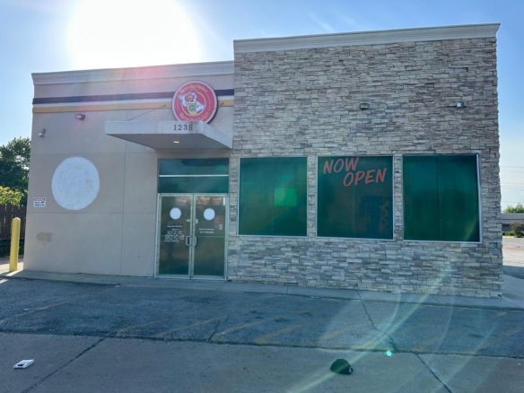 Storefront of a stone-clad restaurant with green-tinted windows; bold NOW OPEN sign on the right window and 1235 above the entrance.